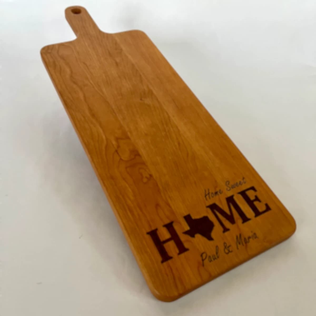 A rectangular wooden cutting board with the phrase "Home Sweet Home" and the shape of Texas laser engraved on it.