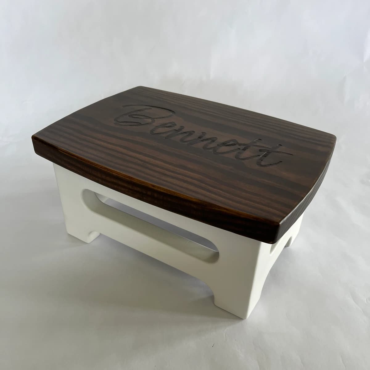A wooden step stool for a child with the name "Bennett" engraved on the top.