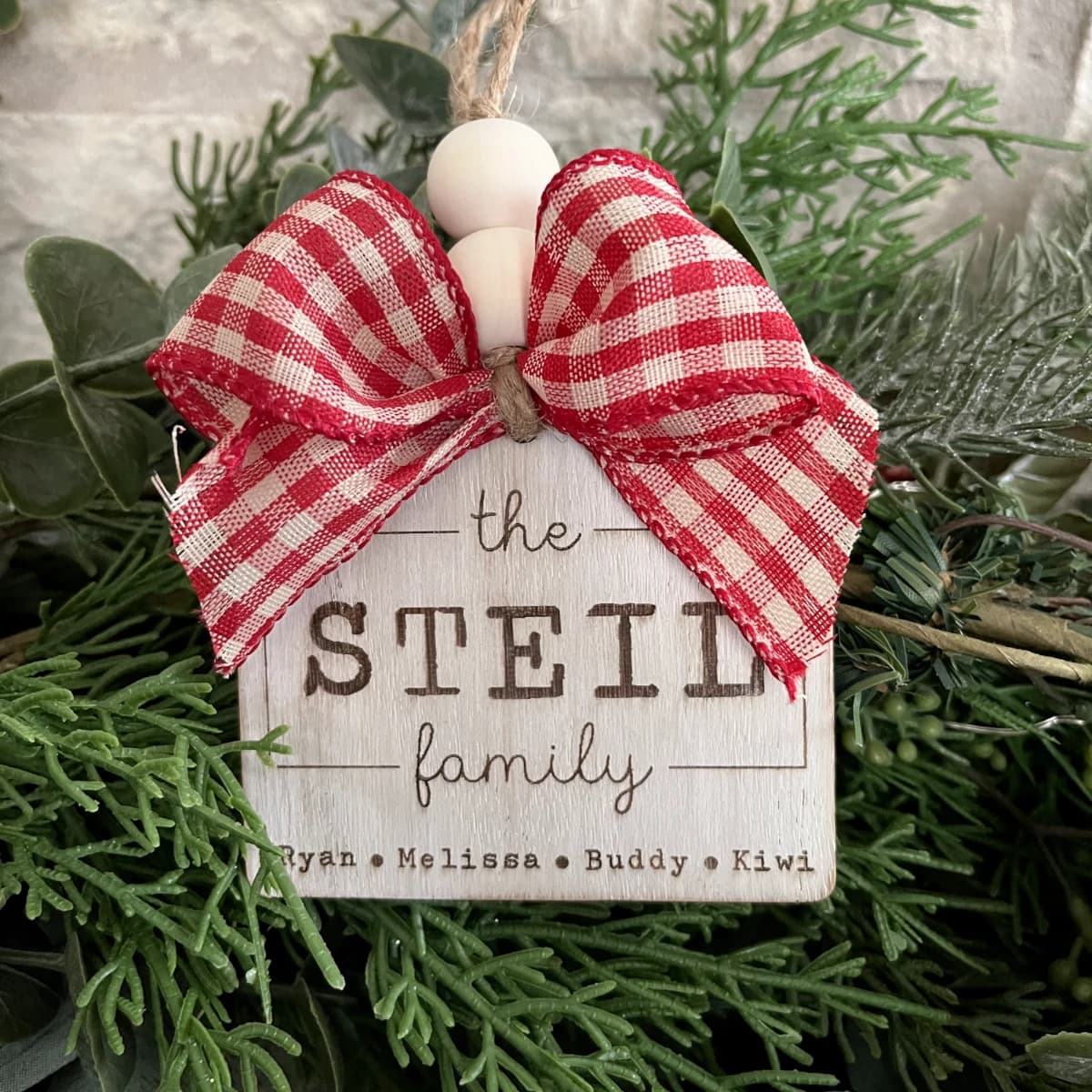 A wooden Christmas ornament laser engraved with text that says The Steil Family, and the names of the family members engraved at the bottom.
