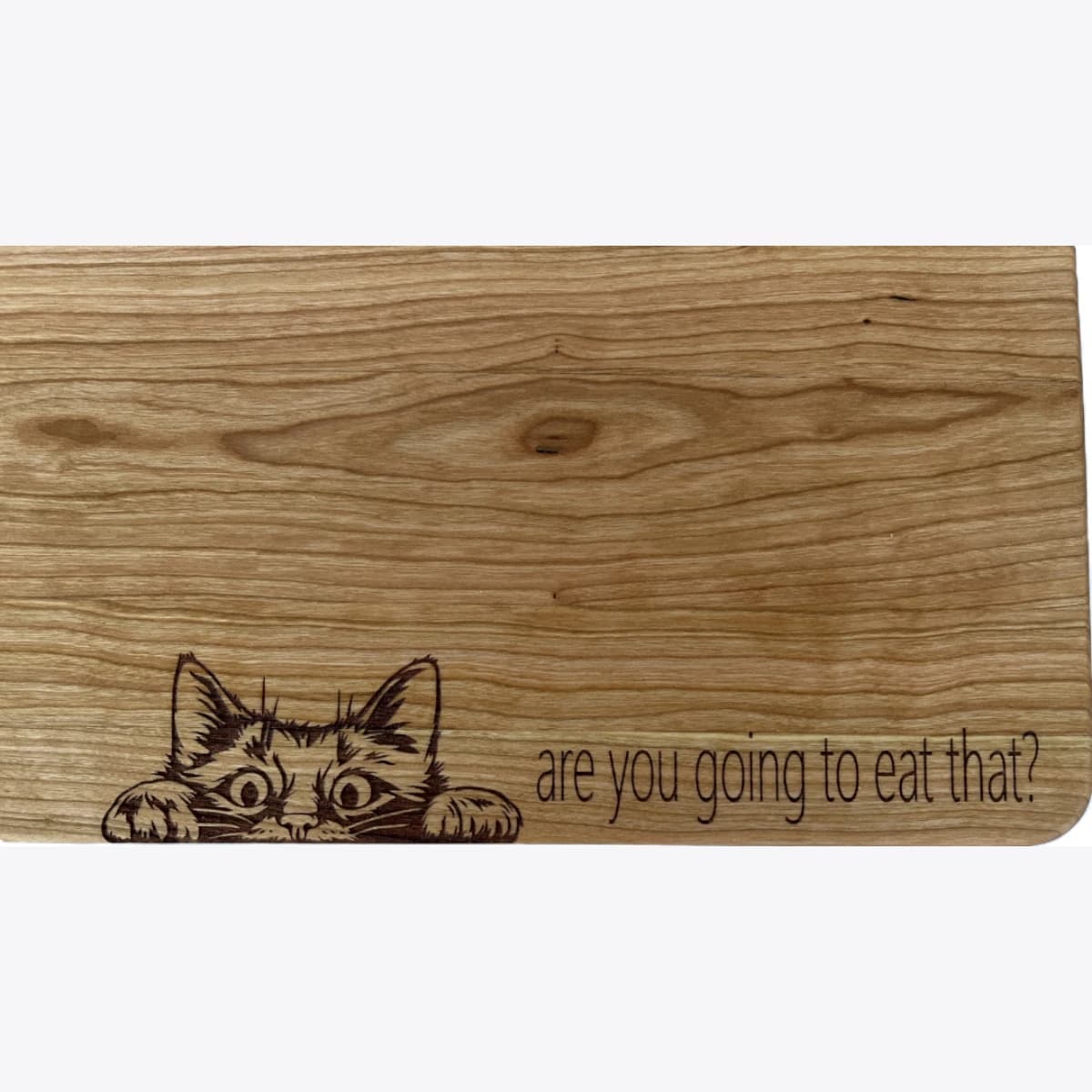 A wooden cutting board laser engraved with an image of a cat peering and text that asks are you going to eat that